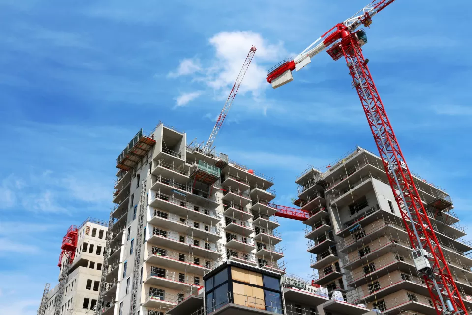 View of top of high-rise apartment building under construction with red and white cranes